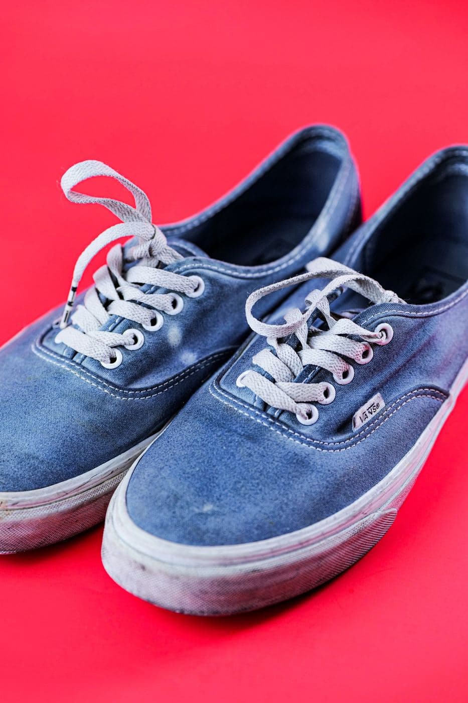 Pair of worn blue canvas pumps on a bright red background