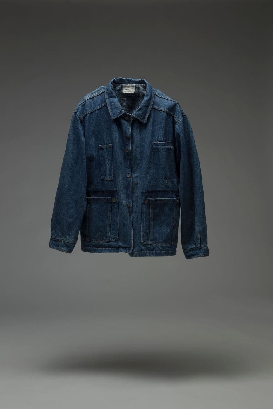 Indigo cotton work jacket with four pockets against a grey background