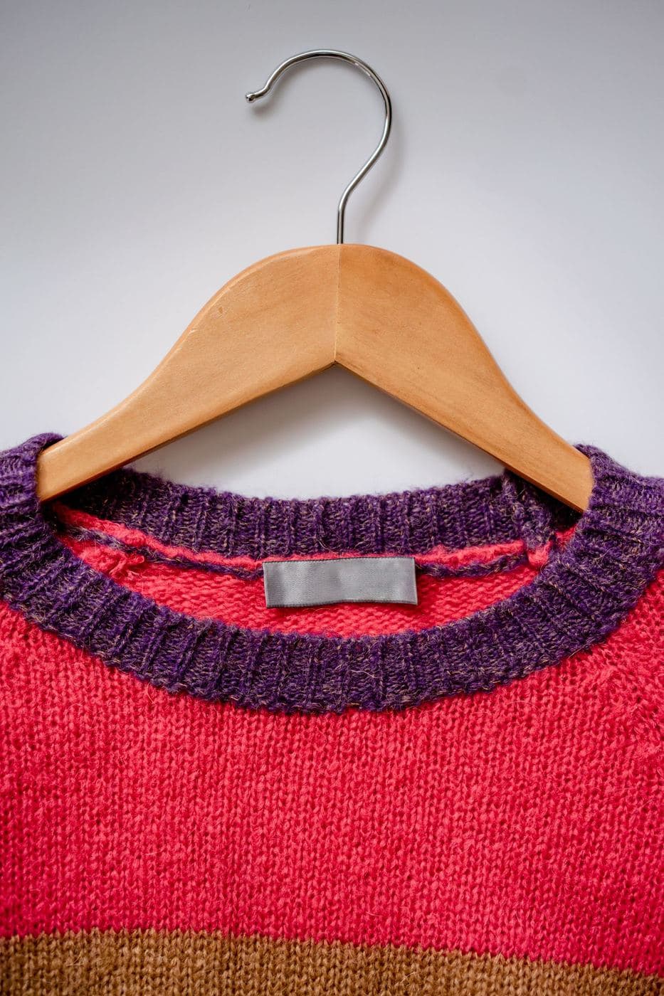 Raspberry pink knitted jumper with a purple neckline on a wooden hanger
