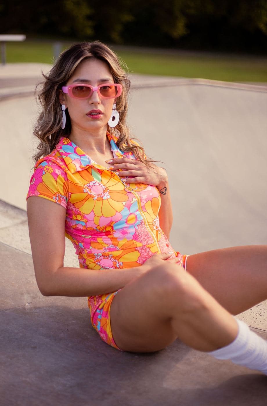 Woman in pink sunglasses at a skatepark wearing a bright floral shirt and shorts set