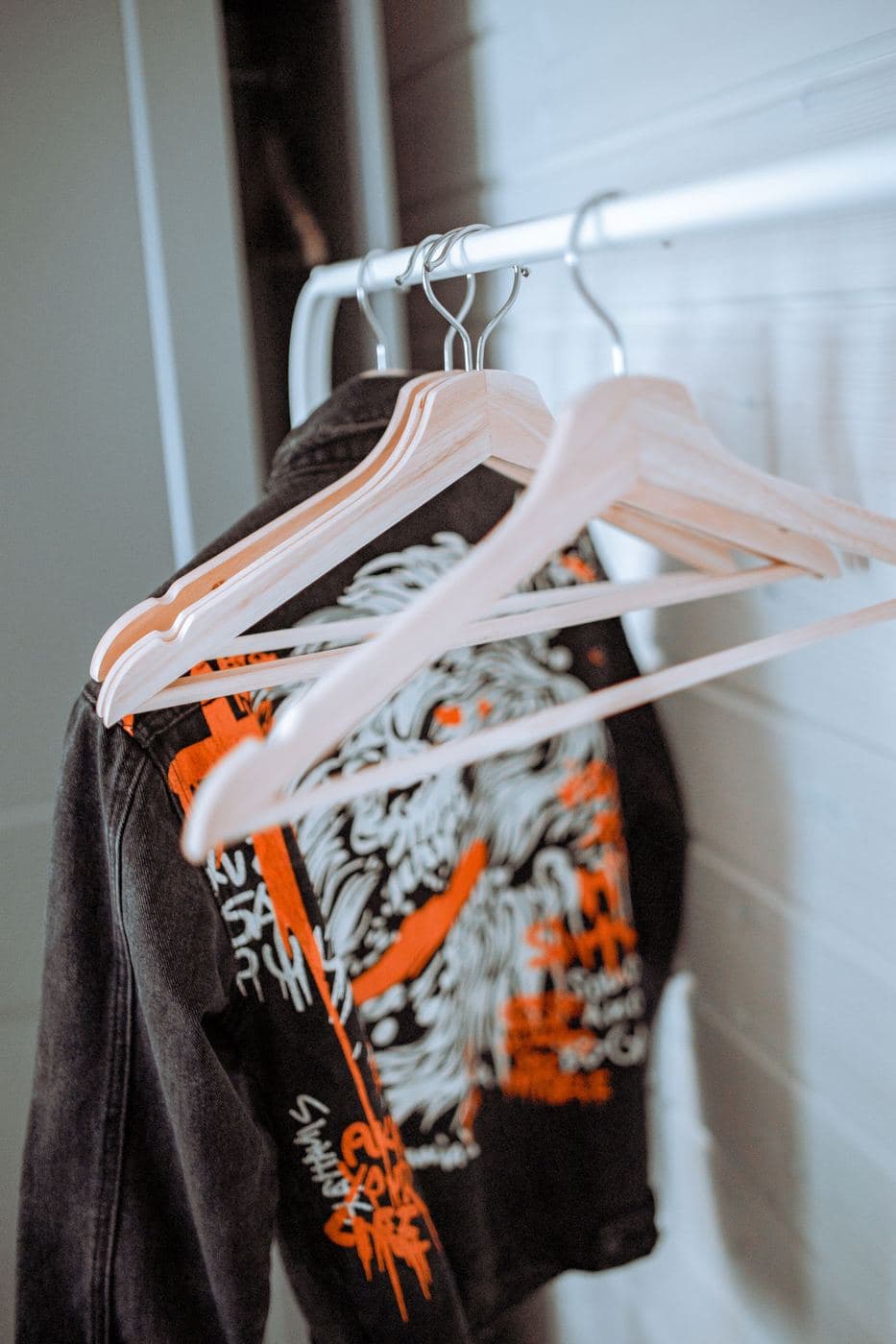 Black jacket with bold orange and white graphic print on white hangers