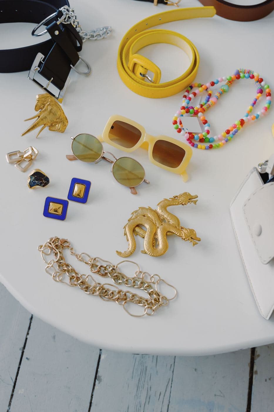 Colourful beaded bracelets, gold chains, sunglasses and belts on a white table