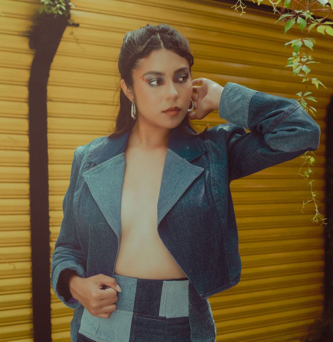 Woman against a yellow shutter wearing a cropped two-tone patchwork denim jacket