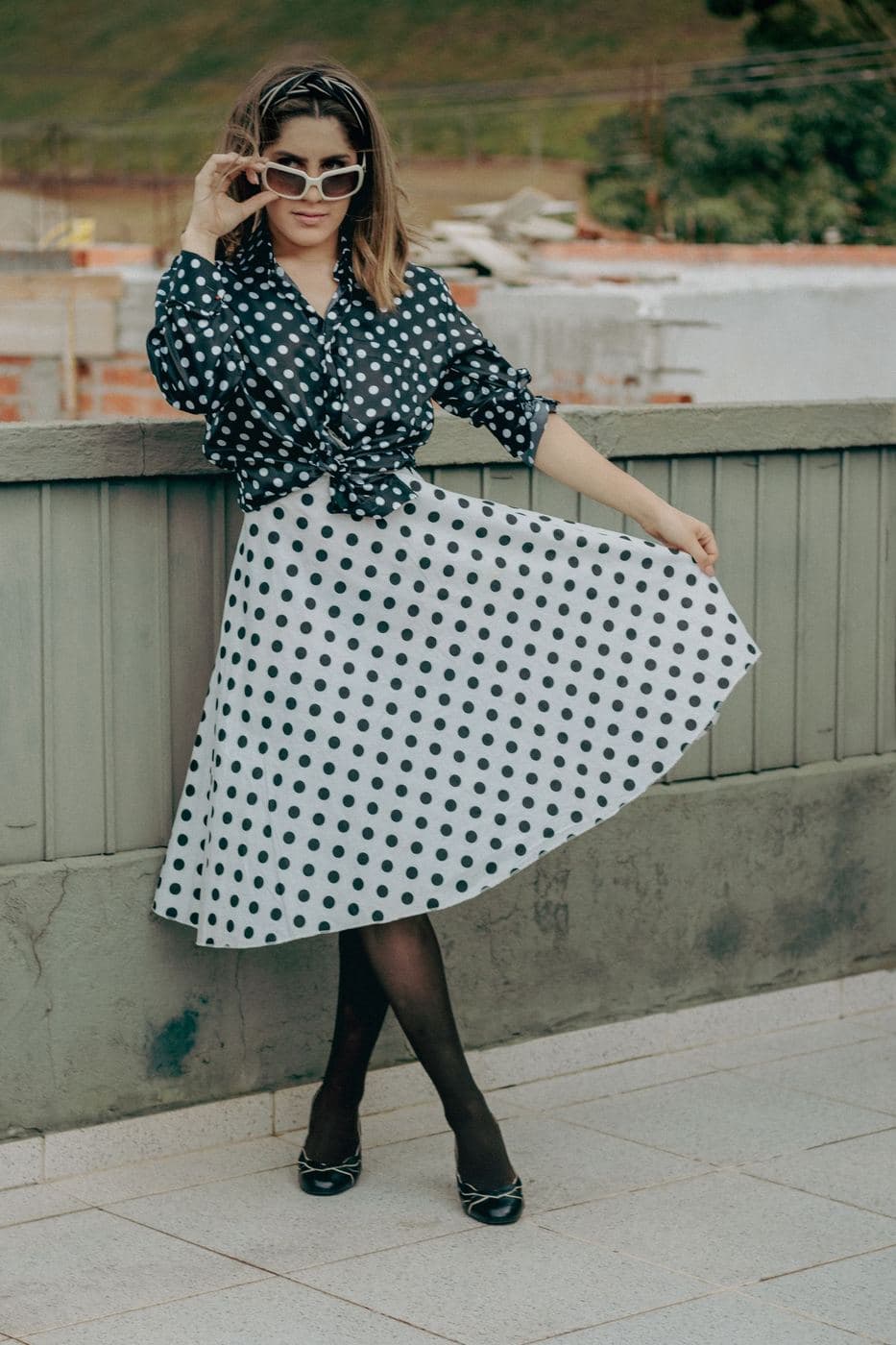 Woman in sunglasses holding out the full skirt of a black and white polka dot dress