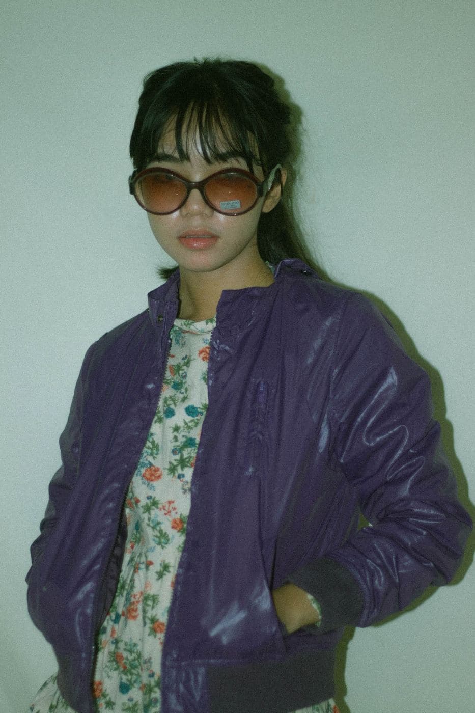 Woman in large sunglasses wearing a shiny purple bomber over a floral dress