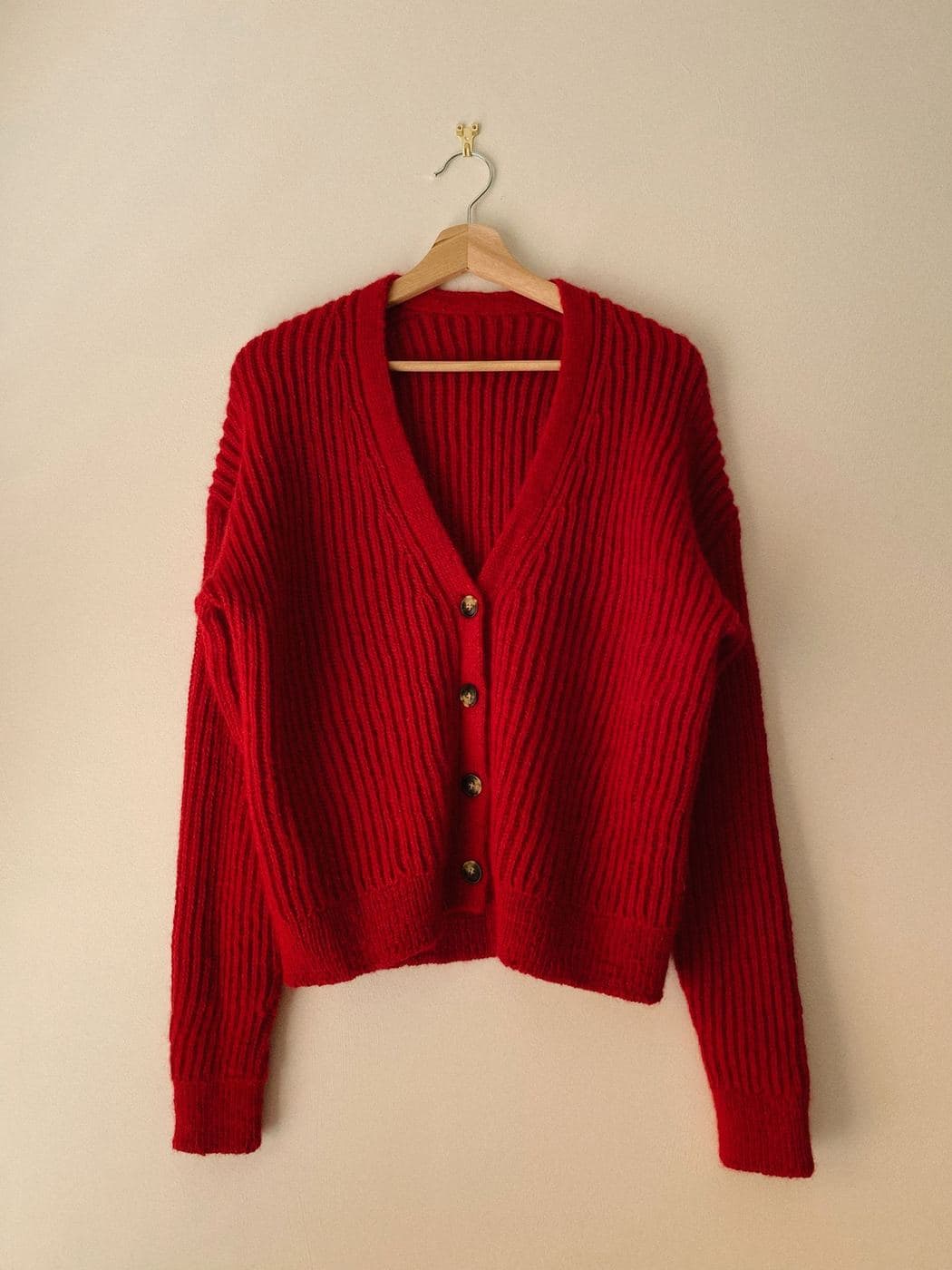 Bright red chunky knit cardigan hanging against a cream wall