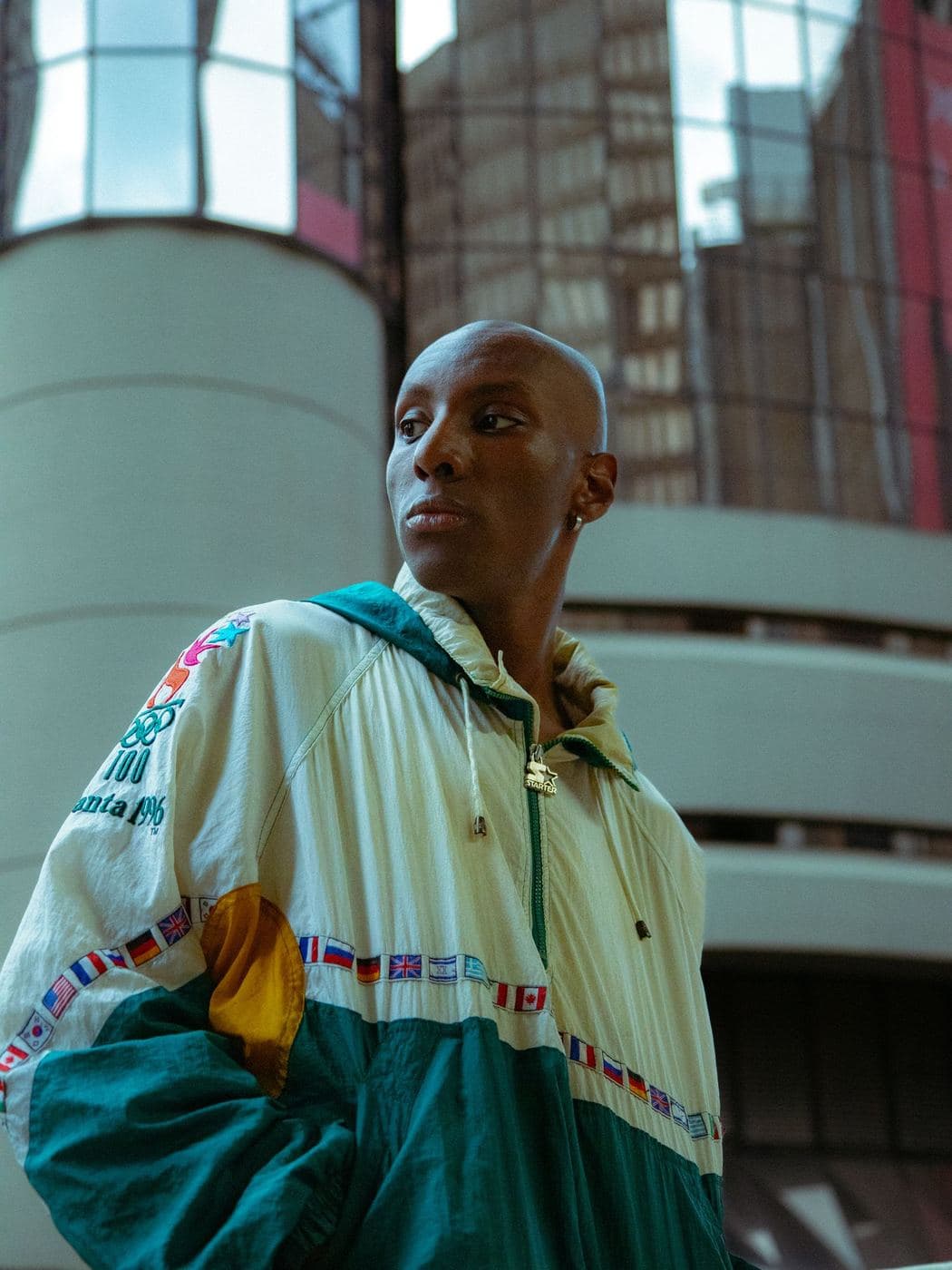 Woman in a cream, teal and red 90s hooded track jacket in front of glass buildings