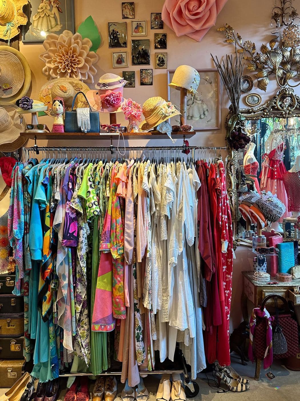 A packed rail of bright vintage clothes under hats and handbags